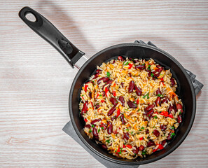 rice with red beans and vegetables in a frying pan on wood table