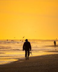 Silhouette of a fisherman walking through waves along the coast at sunset.