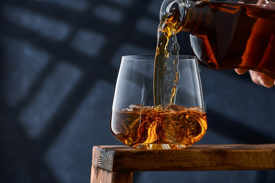 Crystal Glass Of Whiskey With Ice On A Wooden Counter, In A Glass Of Whiskey Poured From A Bottle.