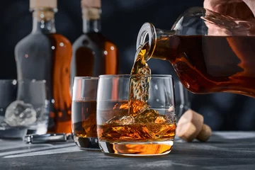 Poster Im Rahmen Zwei Gläser Whisky mit Eis auf einem Betontisch, ein Glas Whisky wird aus einer Flasche gegossen. © Александр Кузьмин