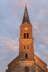 Fototapeta na wymiar Kirchturm im Abendlicht vor Wolke und blauem Himmel