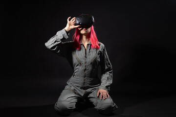 young woman with pink hair and in a jumpsuit uses virtual reality glasses, is in the game,