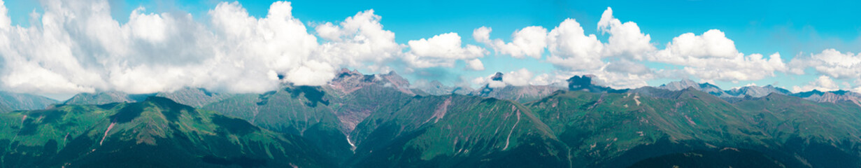Fototapeta premium Panorama of the mountain range on the horizon. High peaks covered with clouds.