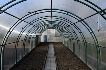 Freshly dig up empty beds in a greenhouse of polycarbonate. The track is lined with tiles. Neat beds.