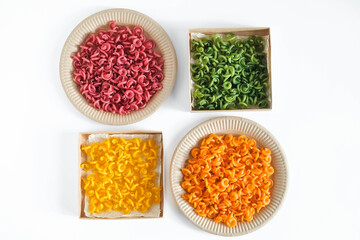 Multicolored pasta in a disposable kraft paper plates and boxes on a white background. Top view. Copy, empty space for text