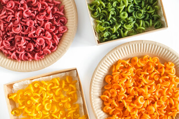 Multicolored pasta in a disposable kraft paper plates and boxes on a white background. Top view. Copy, empty space for text