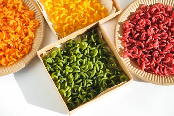 Multicolored pasta in a disposable kraft paper plates and boxes on a white background. Top view. Copy, empty space for text