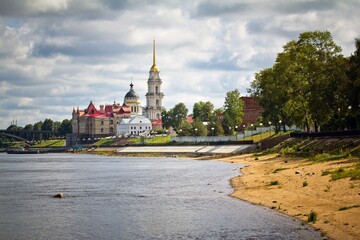 Obraz premium The embankment of the Volga river in the foreground, Transfiguration Cathedral and Historical museum against cloudy sky in summer in Rybinsk, Yaroslavl Oblast, Russia.