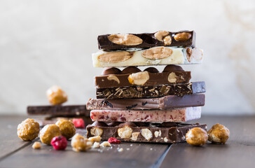 Stack of white, milk and dark chocolate with caramelized hazelnuts and berries on the wooden table