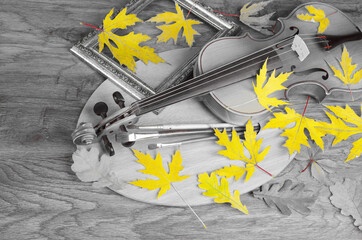 Violin, bow, art palette, brushes and autumn maple leaves on the table.
