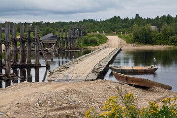 The wooden road bridge across river Vaga near the village Klopovskaya and wooden constructions in the water in summer, Velsky District, Arkhangelsk region, Russia.
