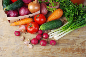 Appetizing vegetables, tomatoes, cucumbers, carrots, onions, garlic, peppers, radishes on a wooden table.