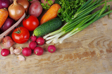 Appetizing vegetables, tomatoes, cucumbers, carrots, onions, garlic, peppers, radishes on a wooden table.