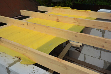Building the roof frame with ceiling joists and rafters over the walls from autoclaved aerated concrete of a home addition construction using a vapor barrier membrane.