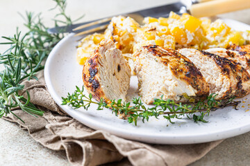 Oven baked or grilled spicy chicken breast with pumpkin and aromatic herbs on a ceramic plate on concrete background. Healthy food.