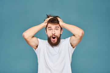 Fototapeta na wymiar A bearded man in a white T-shirt gestures with his hands emotions blue background