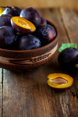 Blue plum in a bowl on a wooden table. Plums in a cut. Top view, place for text. Fruit background with copy space. Still life food.