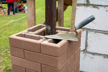 Construction of a brick fence using clinker bricks and cement with a columnar Foundation. Bricklaying close up.