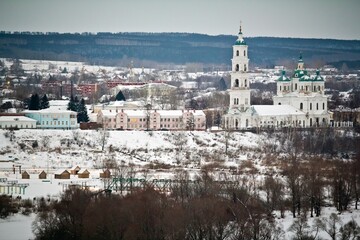 The cityscape of Yelabuga in winter: Shishkin house museum and Spassky cathedral in snowy weather and big forest in the background.