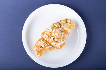 Croissant with almonds on a white plate.