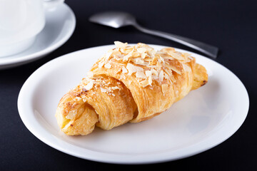 Croissant with almonds on a white plate.
