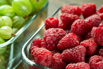 Fresh berries of gooseberries, raspberries and red currants in a glass dish on a wooden table. The concept of healthy food