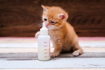 Little redhead  with a sick eye with milk in  a bottle sitting on a wooden table .  Virus and bacteria.