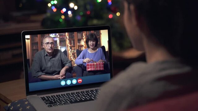 Confined Family celebrating Christmas apart. Video conference call with parents during X-mas holidays. Opening a present distance apart due to the coronavirus pandemic