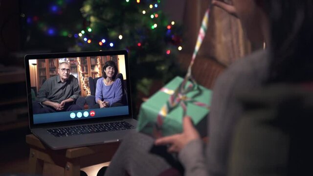 Family celebrating Christmas through a Video call. Parents online celebrating with family during X-mas holidays. Opening presents. Coronavirus celebrations maintaining the distance.

