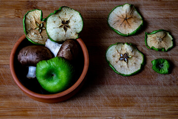 Green dried apple slices and brown mushrooms in the brown plate and on the brown wooden chopping table background