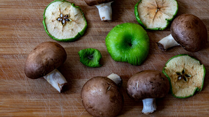 Champignon mushrooms and green dried apple on the wooden board