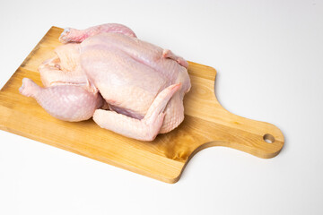 The raw chicken carcass meat on the wooden chopping board 