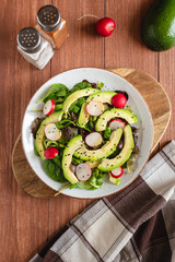 Organic healthy salad of avocado, radish and mixed lettuce with olive oil and black cumin