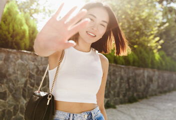 Beautiful asian woman covering herself from camera and smiling, posing in trendy outfit, walking in...