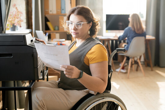 Young Disable Office Worker Looking At Paper While Sitting By Xerox Machine