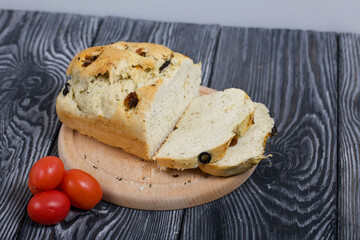 Focaccia bread with olives and sun-dried tomatoes. Several red tomatoes are nearby. On pine boards.
