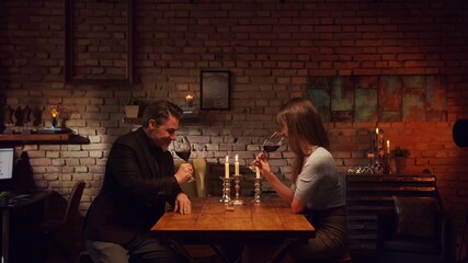 Elegant couple having romantic dinner at home, sitting at table in living room drinking red wine. Stay at home concept.