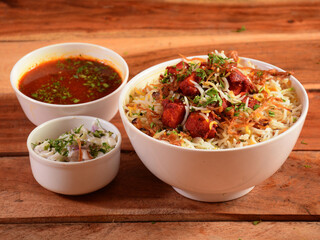 Veg Paneer tikka Biryani with mixed veggies like Paneer, Potato, Carrots, Peas cooked along with spiced rice and served with onion raita and curry, selective focus