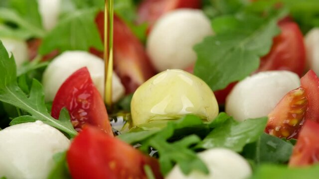 caprese salad. pour olive oil on Italian salad Caprese with mini mozzarella, tomatoes cherry and arugula