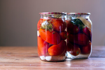 Homemade pickled tomatoes in glass jars on rustic wooden background. Fermented tomatoes in transparent glass. Homemade canned tomatoes.