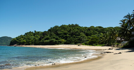 Beautiful landscape of the mexican pacific coast in a sunny day with a blue and clear sky, trees, palms and green hills, some waves and sand in the beach