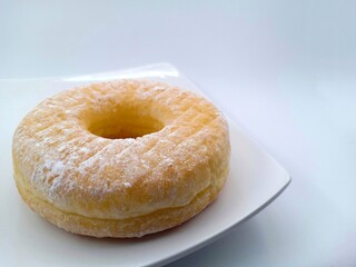 A glazed yeast-raised ring American-style doughnut served on a white plate.  It tastes so sweet and it can also be paired with milk. Isolated on white. It can be used for culinary background