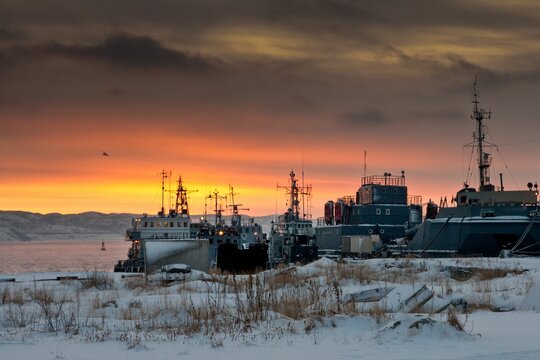 Moored ships in dock of Barents Sea and the ground covered with snow and faded grass in winter in Severomorsk, Russia.