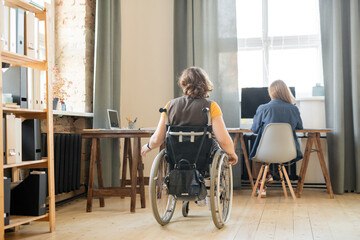 Back view of young disable female in wheelchair moving along one of tables