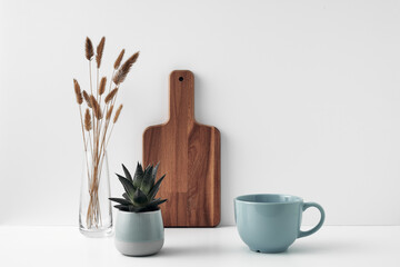 A mug, a potted houseplant, a clear vase and a wooden cutting board. Eco-friendly materials in the decor of the room, minimalism. Copy space, mock up