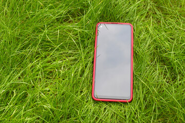 Modern smartphone with a red case on green fresh grass.