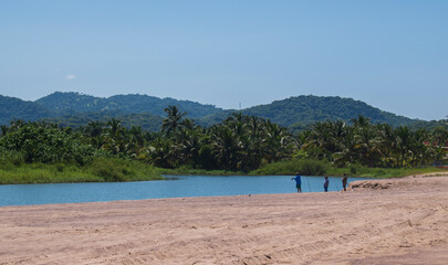 A group of people fishing in a mexican beach of the pacific coast  with a beautiful landscape in the background, and a clear and blue sky of a sunny day