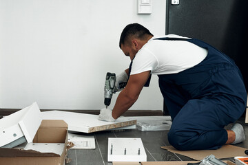 Furniture assembly process. Worker in overalls and white footwear. Using a cordless drill,...