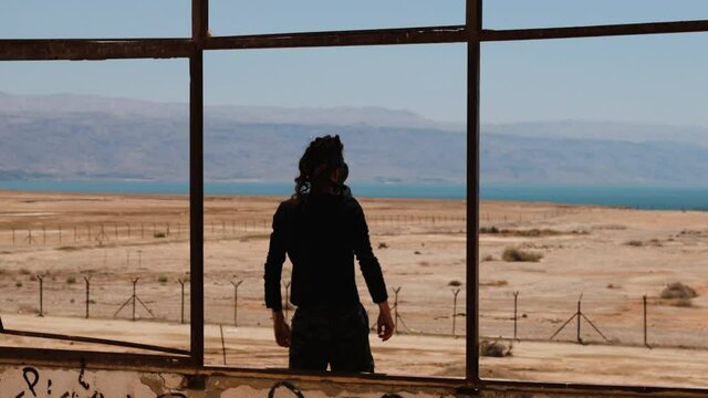 Man with gas mask stretching out his arms in front of an apocalyptic dessert view.