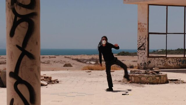 Post apocalypse workout &ndash; man practicing Capoeira between ruins, with a medical mask on his face.